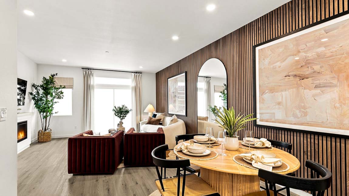 Dining area with round wood table and four chairs overlooking a contemporary living room with fireplace and accent wall.