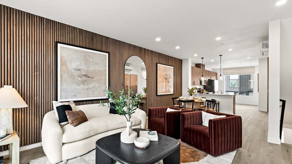 Stylish open living space with modern seating, wood feature wall, dining area, and kitchen with breakfast bar.