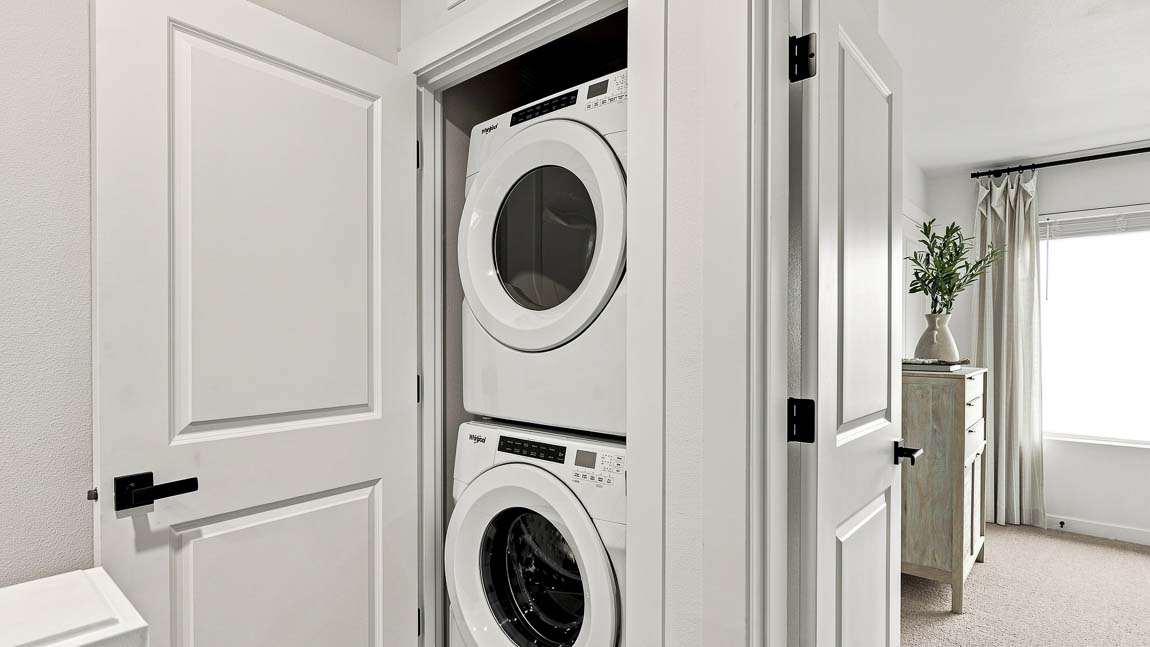 Stacked white front-loading washer and dryer in a recessed laundry closet beside a bedroom doorway.