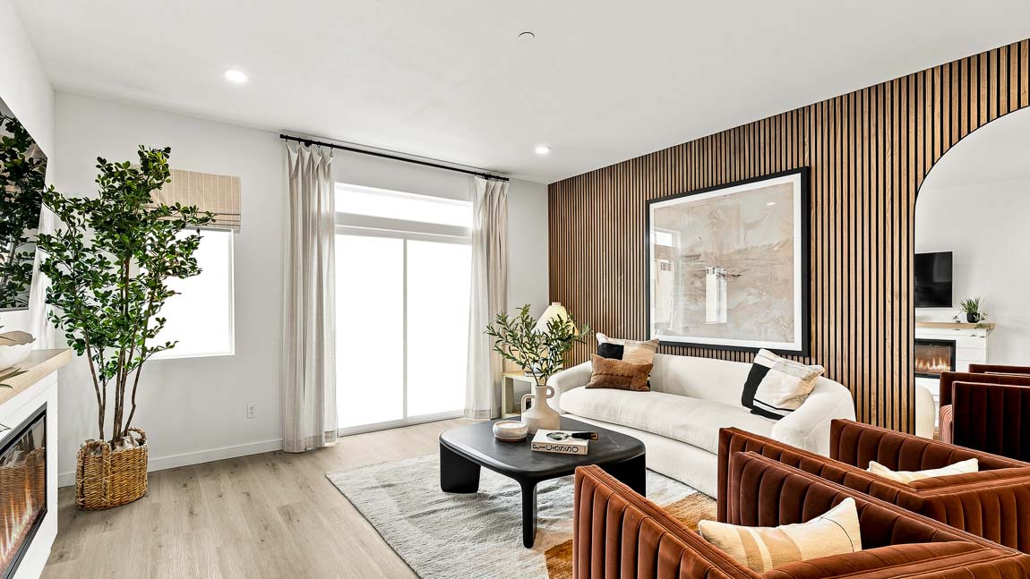 Living room with white sofa and rust-colored lounge chairs around a black coffee table, wood slat accent wall with large artwork and arched mirror, and bright windows.