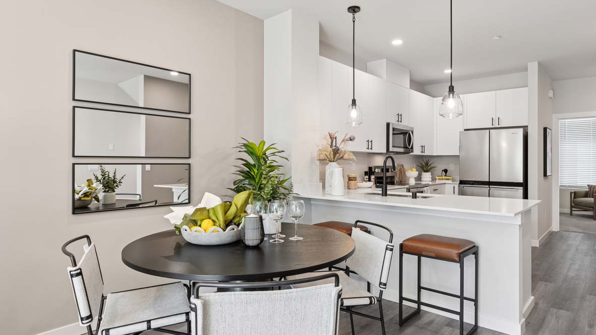Dining area adjacent to a white kitchen featuring a round dining table, pendant lighting, large island, and stainless steel appliances.