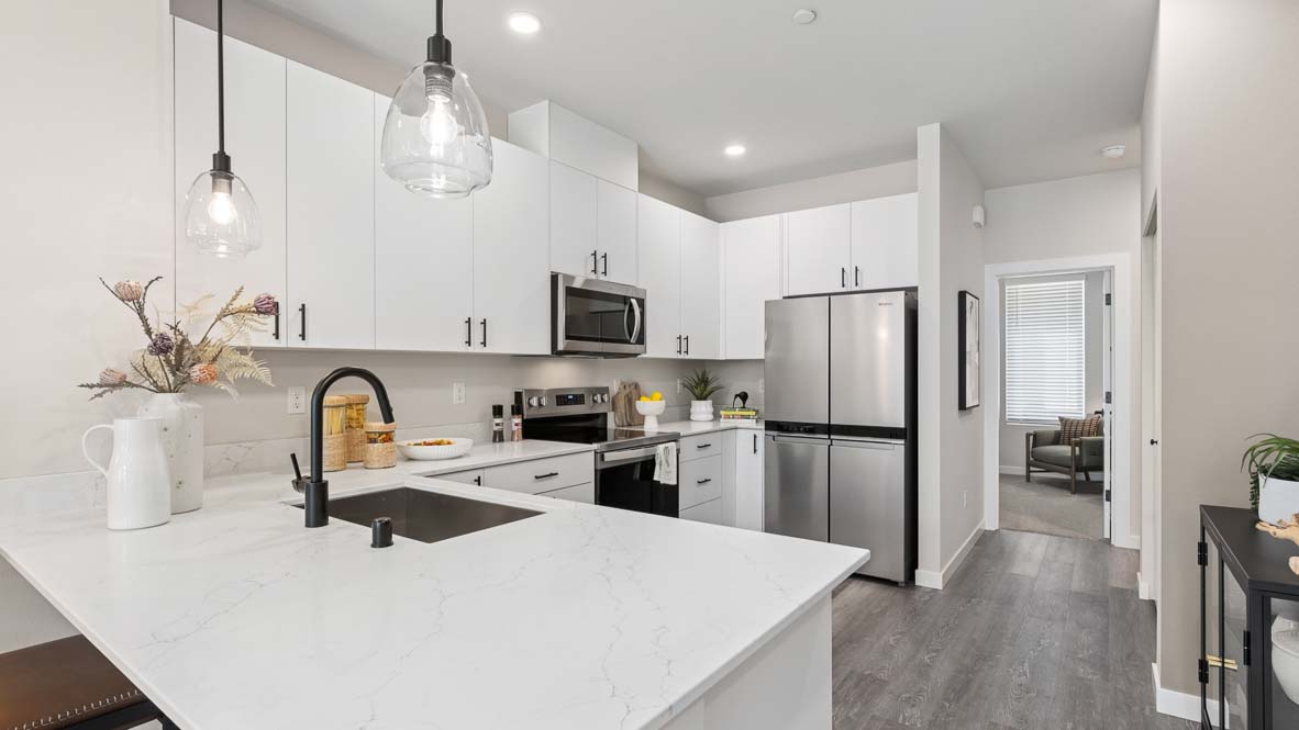 Modern kitchen with white shaker cabinets, quartz countertops, pendant lights, stainless steel refrigerator, and spacious island with sink.