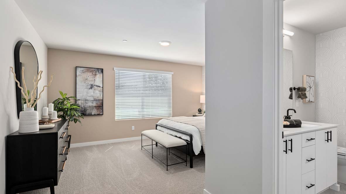 View from the primary bedroom toward the adjoining bathroom, showing a dresser, bed, vanity area, and neutral finishes.