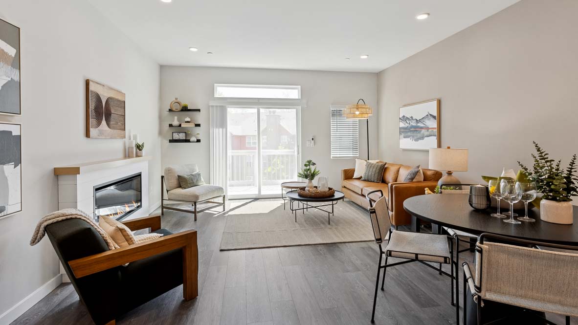 Open living and dining space with a fireplace, sliding glass door to a balcony, leather sofa, dining table, wall art, and gray flooring.