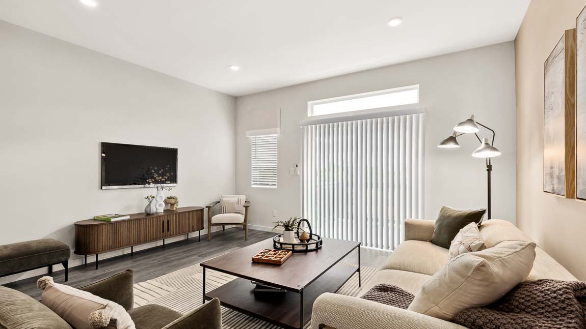 Contemporary living room in a new construction home featuring comfortable seating, a wall-mounted television, luxury vinyl plank flooring, abundant natural light, and sliding glass door access to a private outdoor space.