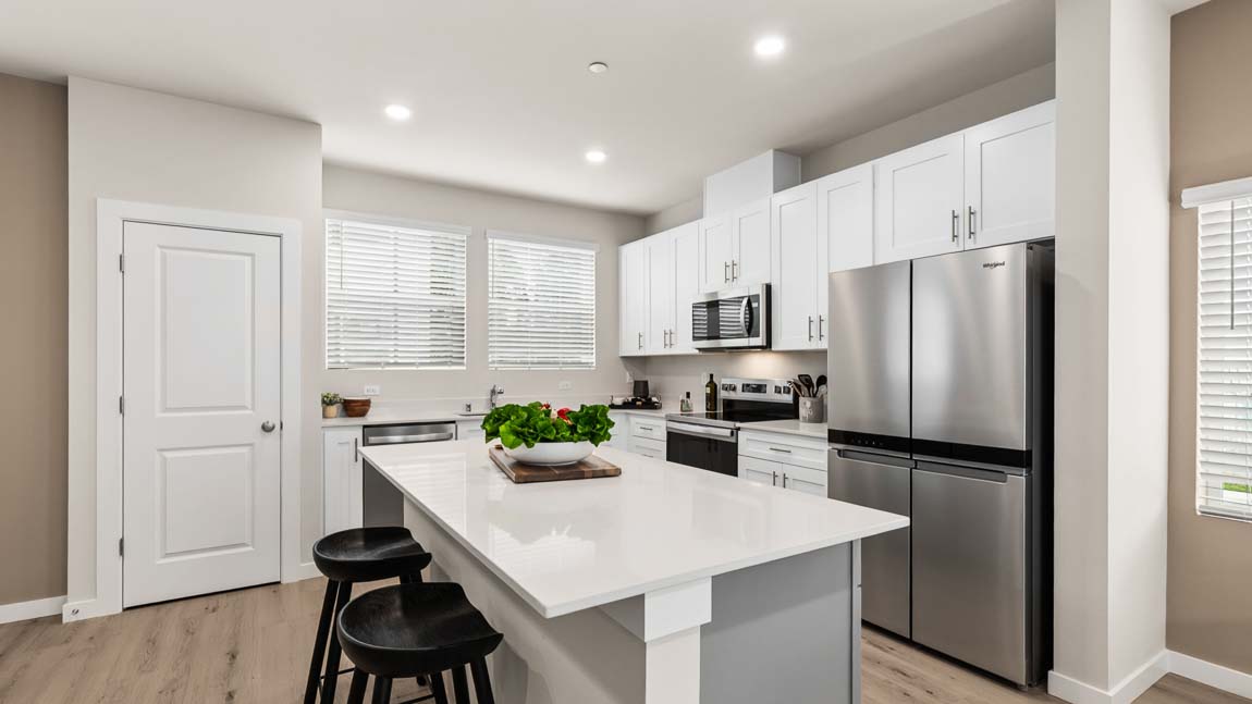 Contemporary kitchen with white shaker cabinets, quartz island, stainless steel appliances, and bar seating for two.