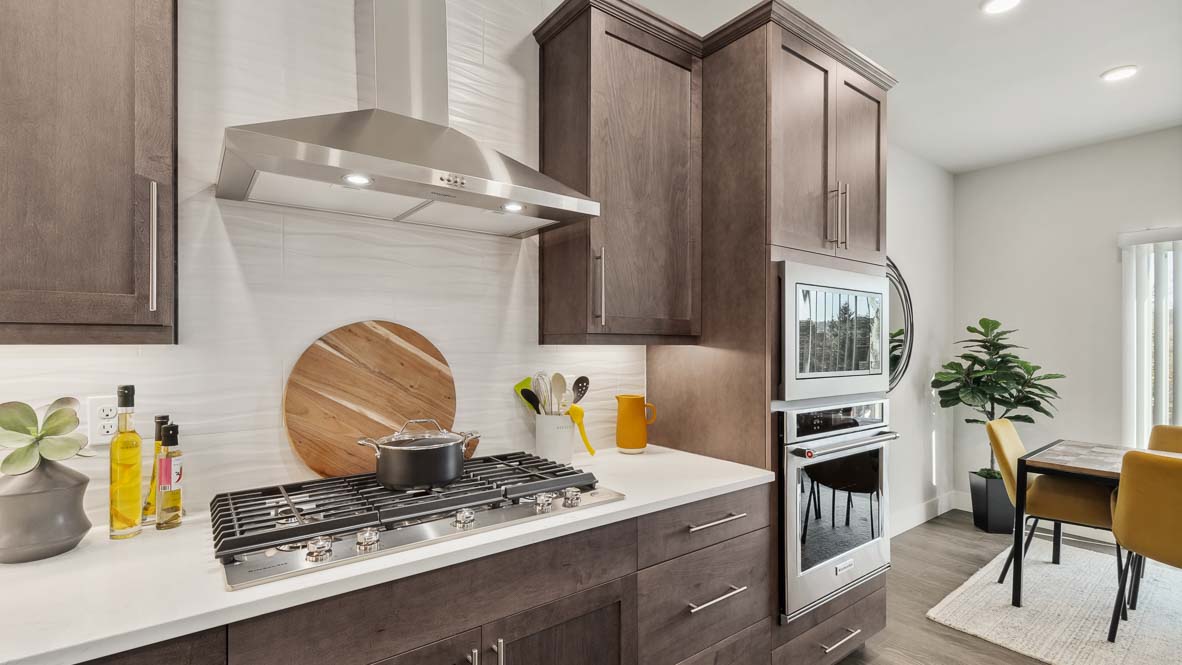 Stainless steel range hood and five-burner gas range with ceramic tile backsplash in kitchen