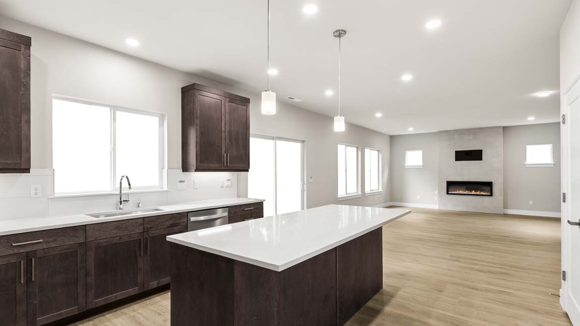 Open-concept kitchen with a large quartz island, dark wood cabinetry, pendant lighting, and adjoining great room with fireplace.