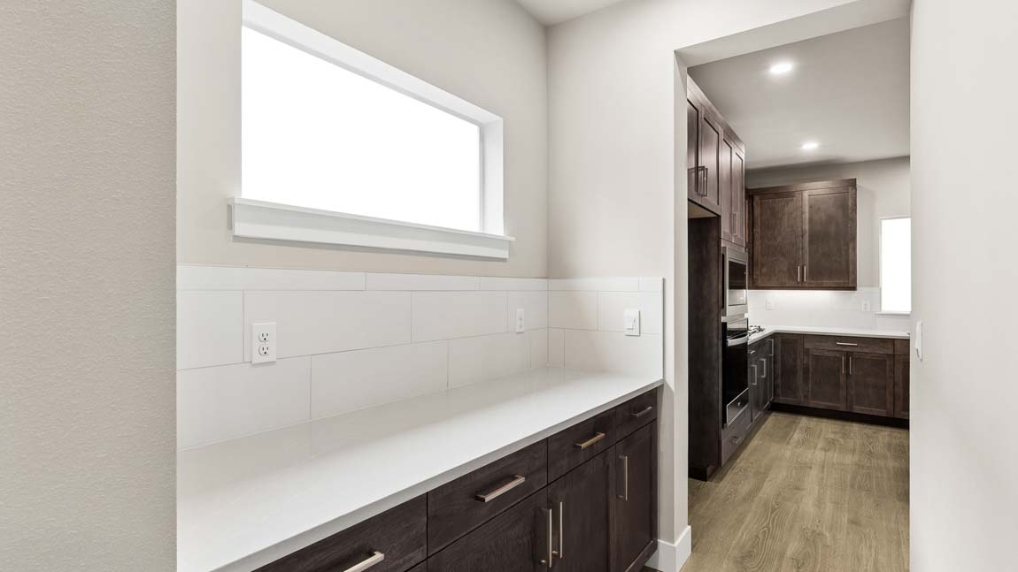 Butler’s pantry with quartz countertop, tile backsplash, dark cabinetry, and access to the main kitchen.