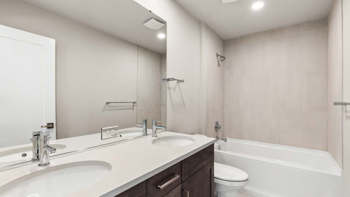 Full bathroom with dual-sink vanity, quartz countertop, large mirror, and tub-shower combination with tiled surround.