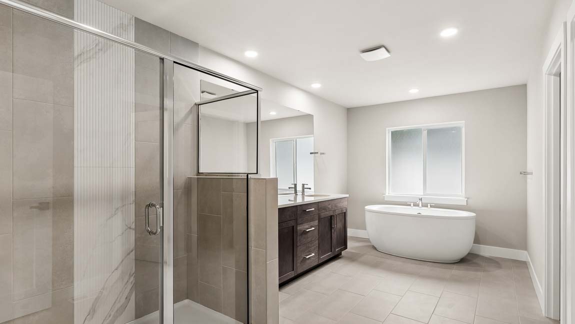 Luxury primary bathroom with frameless glass shower, freestanding soaking tub, dual-sink vanity, and tile flooring.