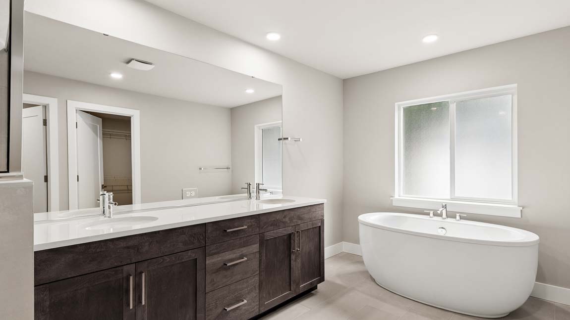 Primary bathroom featuring a dual-sink vanity with quartz countertop and a freestanding soaking tub beneath a large window.