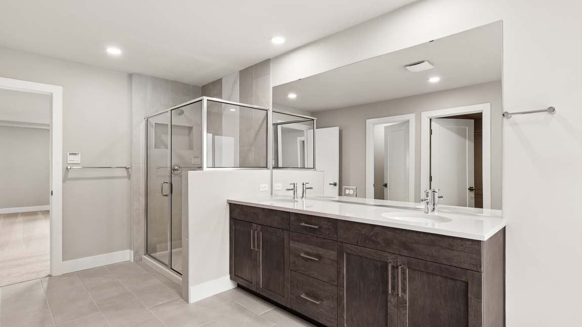 Spacious primary bathroom with dual-sink vanity, quartz countertops, large mirror, glass-enclosed shower, and tile flooring.