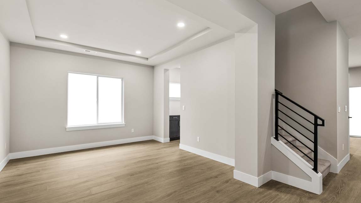 Open living area with wood-look flooring, recessed lighting, staircase with black metal railing, and large window.