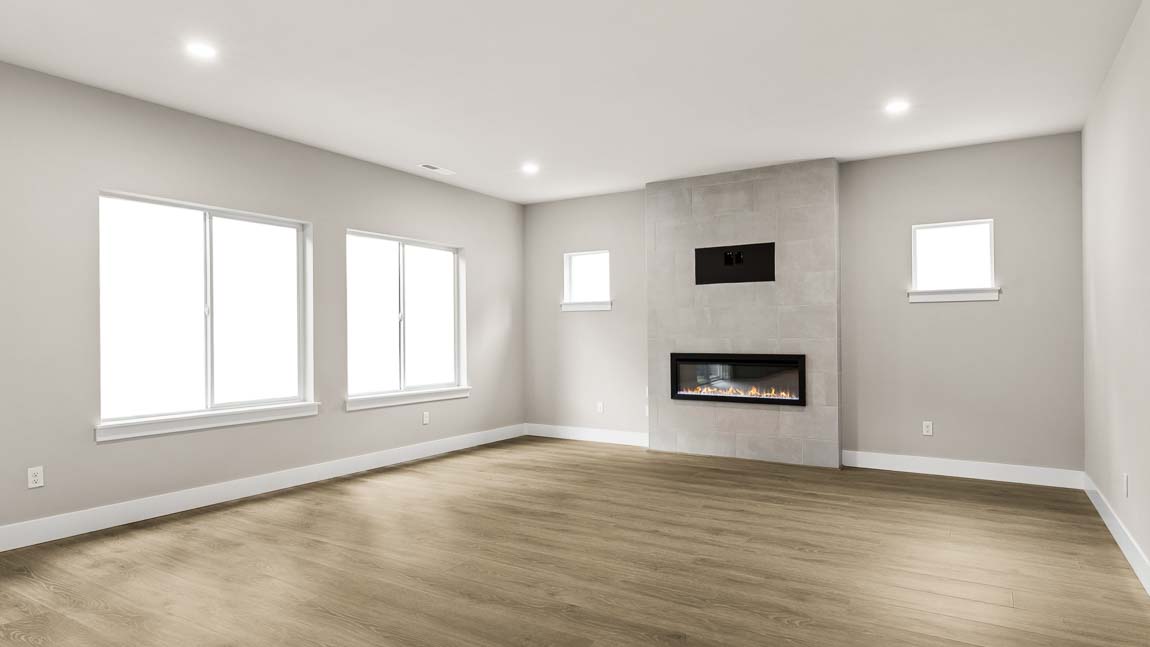 Bright great room featuring wide-plank flooring, multiple windows, and a contemporary gas fireplace with tile surround.