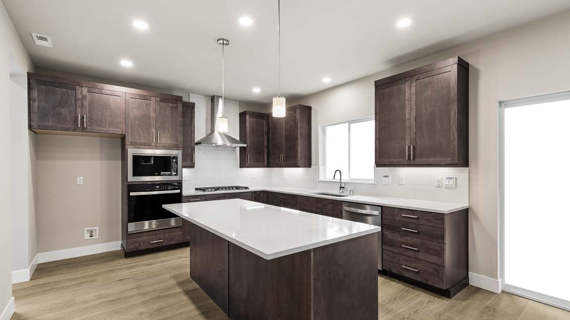 Contemporary kitchen with dark wood cabinetry, large quartz island, stainless steel appliances, recessed lighting, and sliding glass door access.