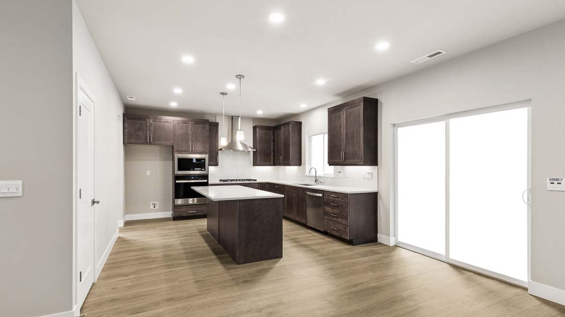 Open-concept kitchen with quartz island, dark shaker-style cabinets, stainless steel range hood, and adjacent staircase with modern railing.