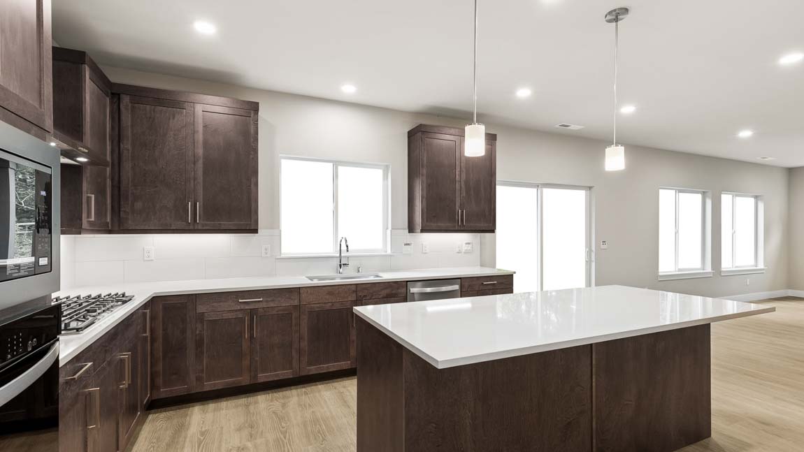 Close-up of a gas cooktop with stainless steel range hood, white tile backsplash, quartz countertops, and dark cabinetry.