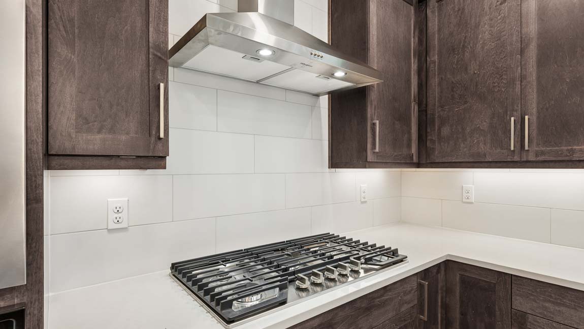 Modern kitchen with oversized quartz island, built-in wall oven and microwave, dark cabinetry, and abundant natural light.