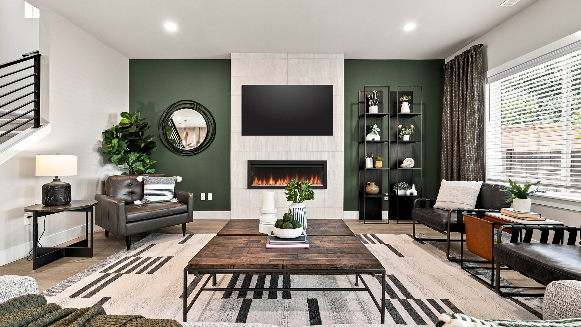 Contemporary living room with fireplace, wall-mounted TV, green accent wall, leather seating, and decorative shelving.