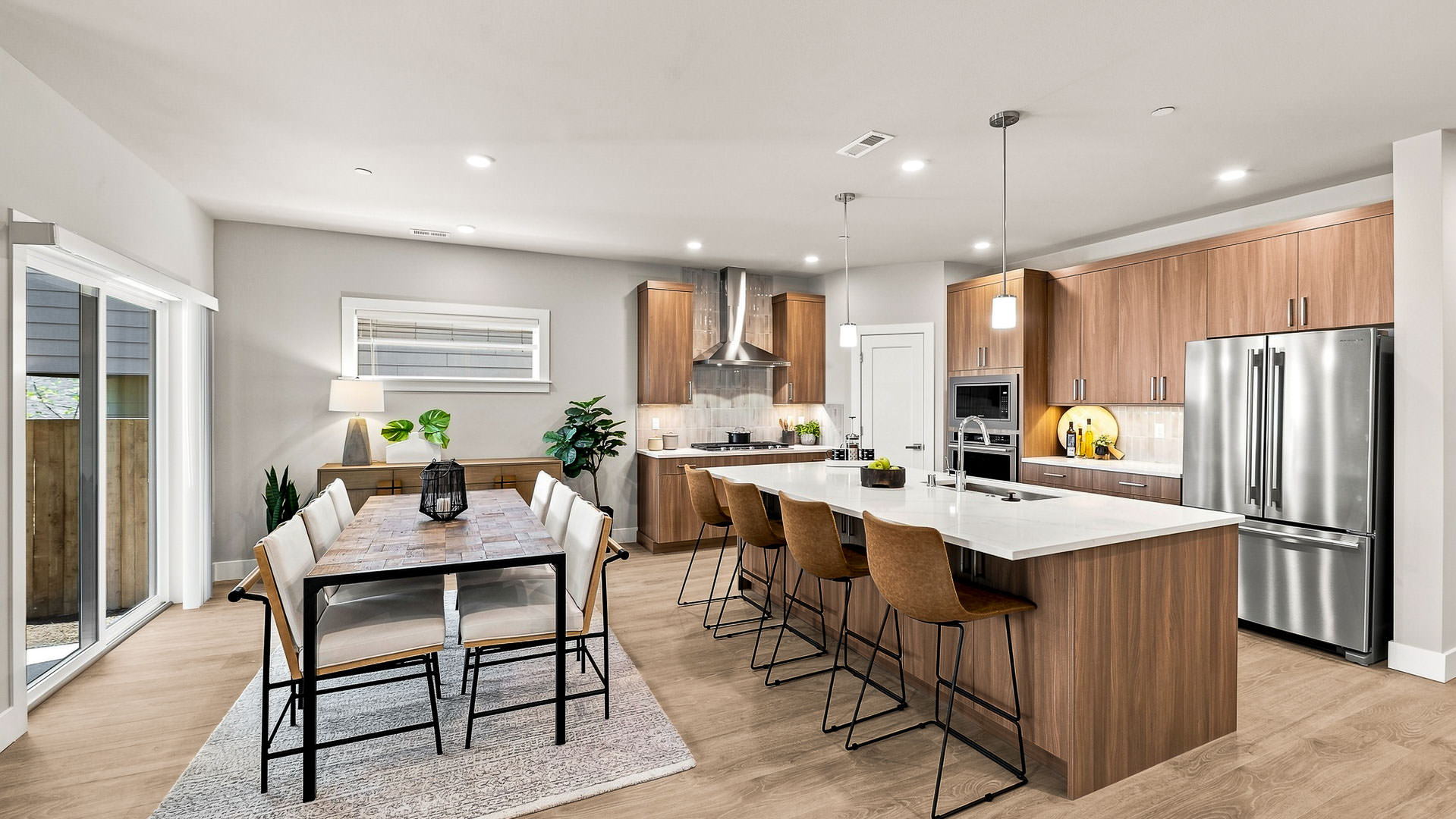 Open-concept kitchen and dining area featuring a large island, pendant lighting, wood cabinets, and stainless steel refrigerator.