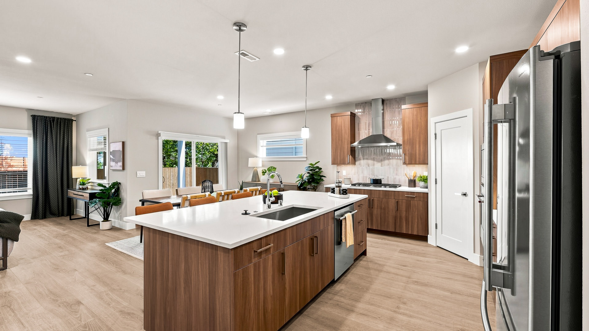 Bright kitchen with oversized island, integrated sink, wood cabinetry, dining area, and sliding glass door.