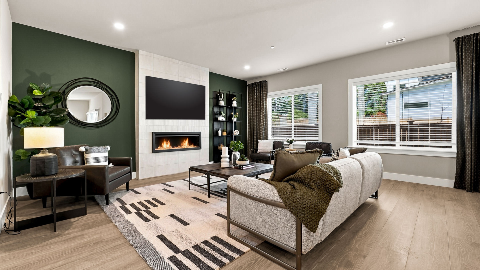 Living room with fireplace, TV, accent wall, sofa, armchairs, and large windows providing natural light.