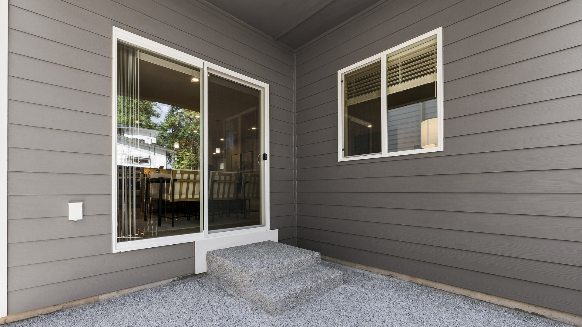 Covered backyard patio with concrete surface, sliding glass door to the dining area, gray exterior siding, and adjacent window.