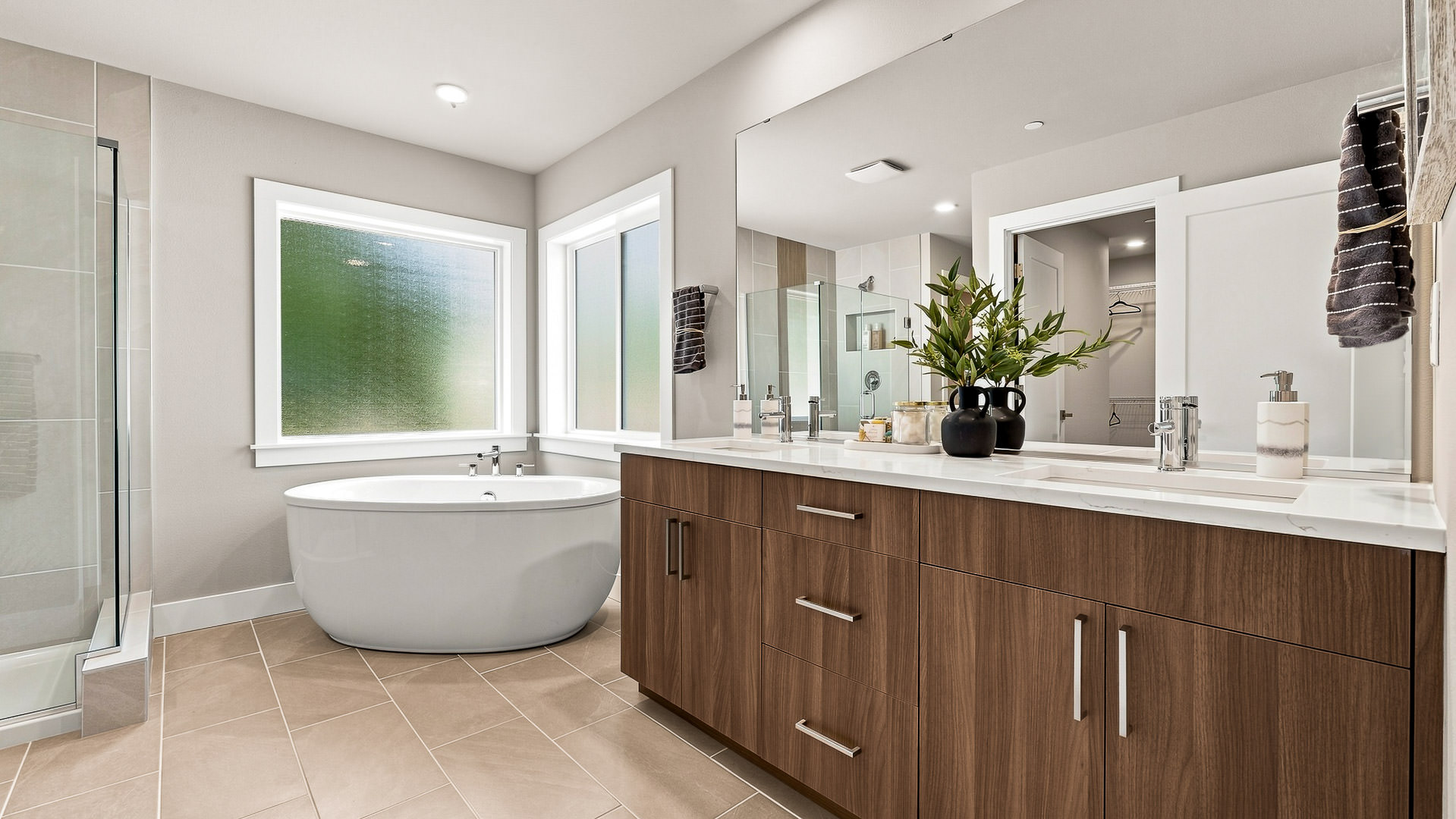 Primary bathroom with double vanity, large mirror, soaking tub, and glass shower enclosure.