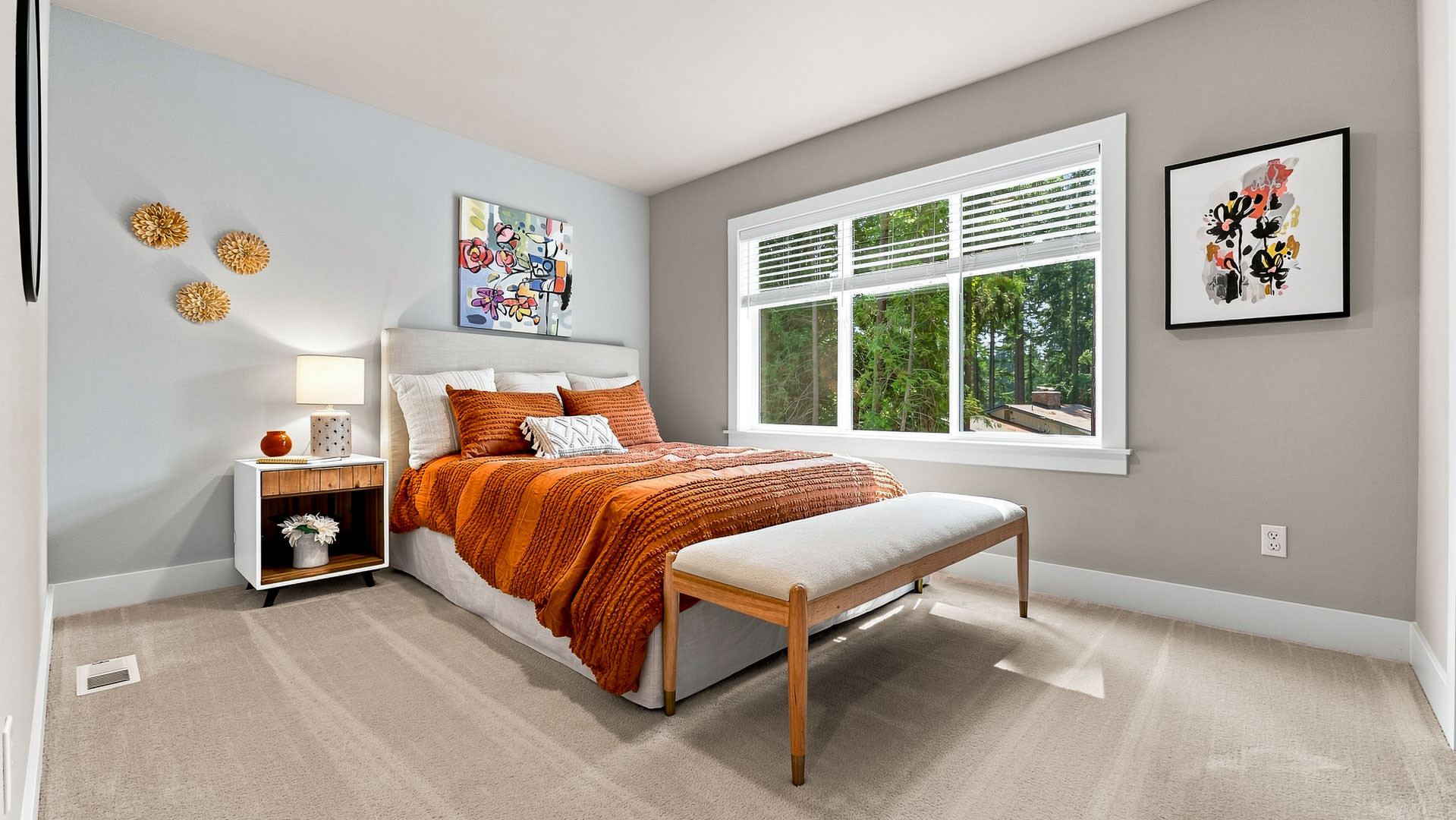 Guest bedroom with upholstered bed, orange bedding accents, artwork, and large window overlooking trees.