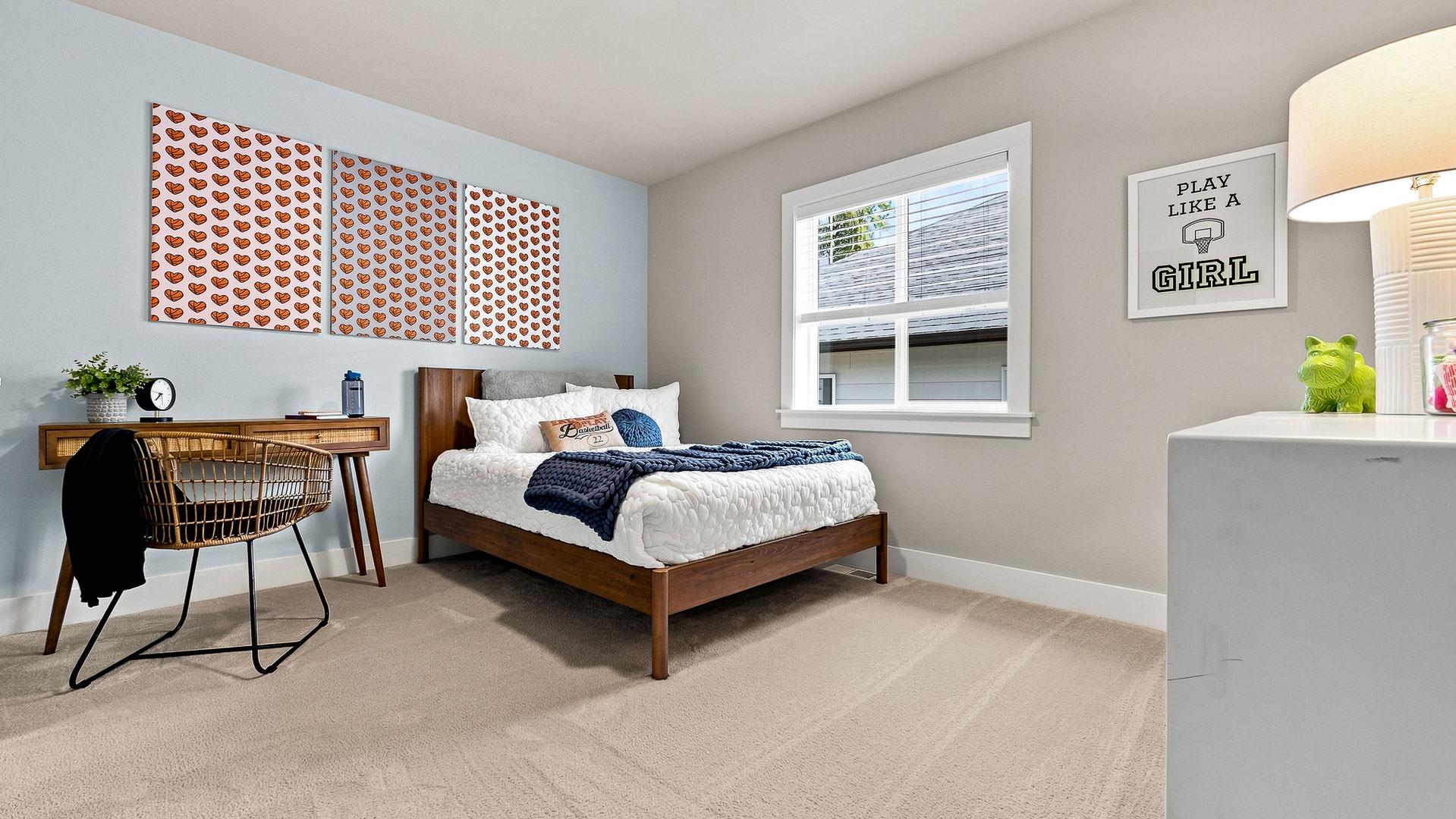 Bedroom with single bed, study desk, woven chair, sports-themed artwork, and bedside dresser.