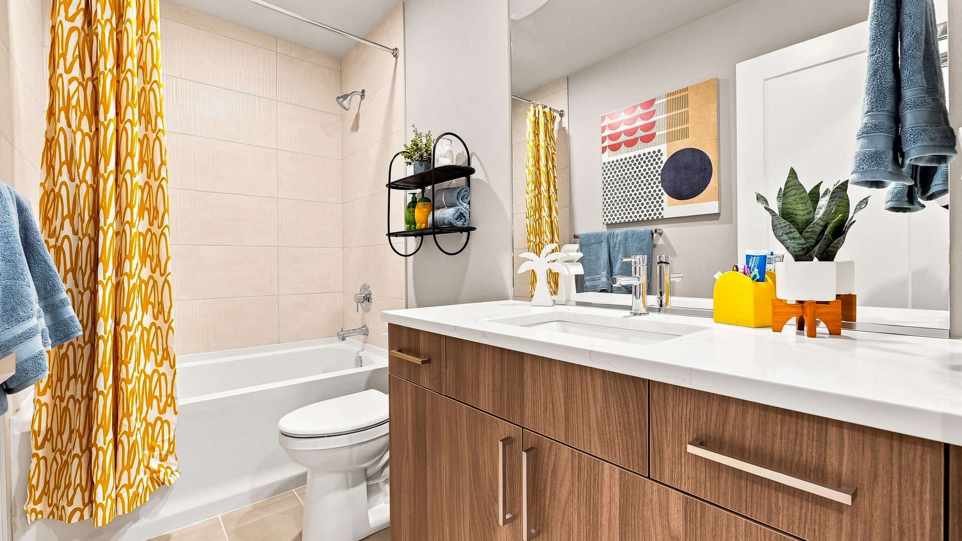 Bathroom with wood vanity, white countertop, colorful shower curtain, and decorative wall art.
