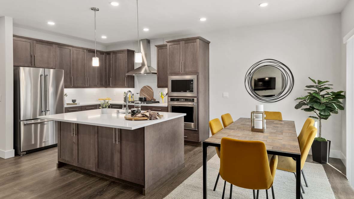 Open kitchen and dining area featuring a large island, stainless steel appliances, wood dining table, and mustard-colored chairs.