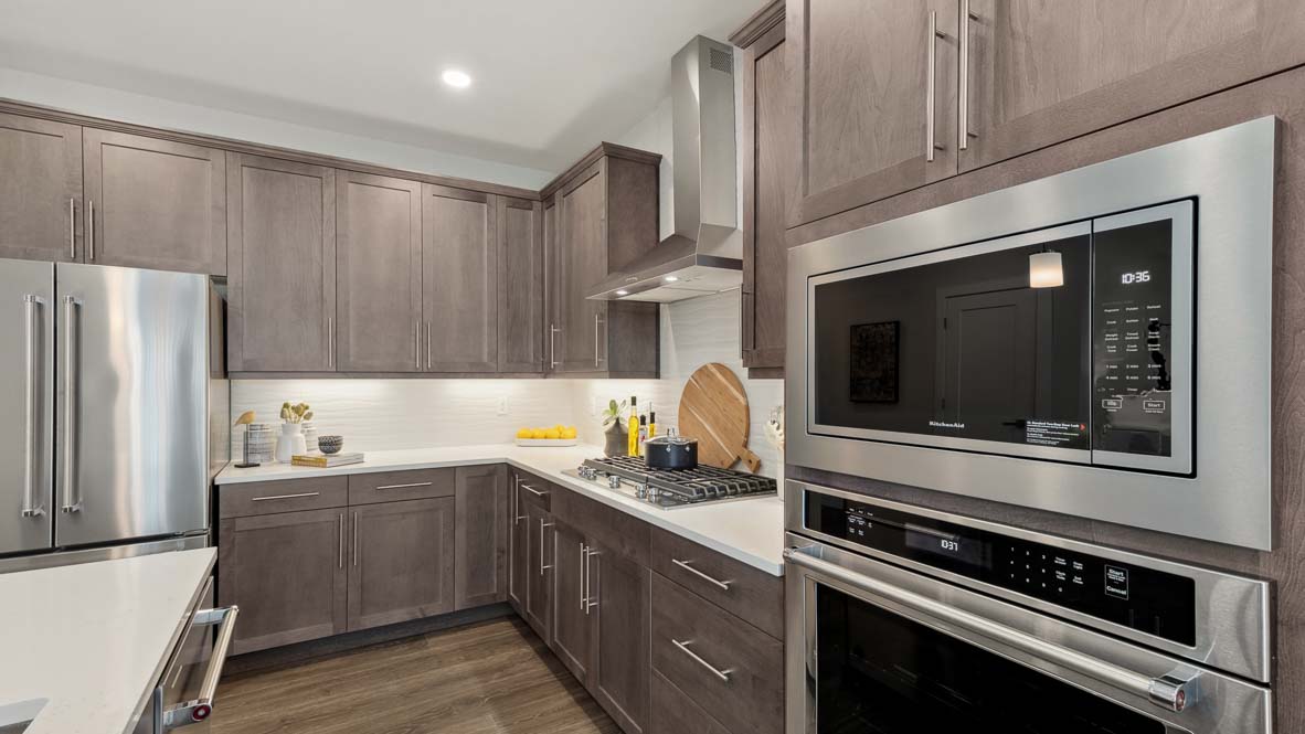 Modern kitchen with built-in microwave and wall oven, gas cooktop, stainless steel range hood, and dark wood cabinets.