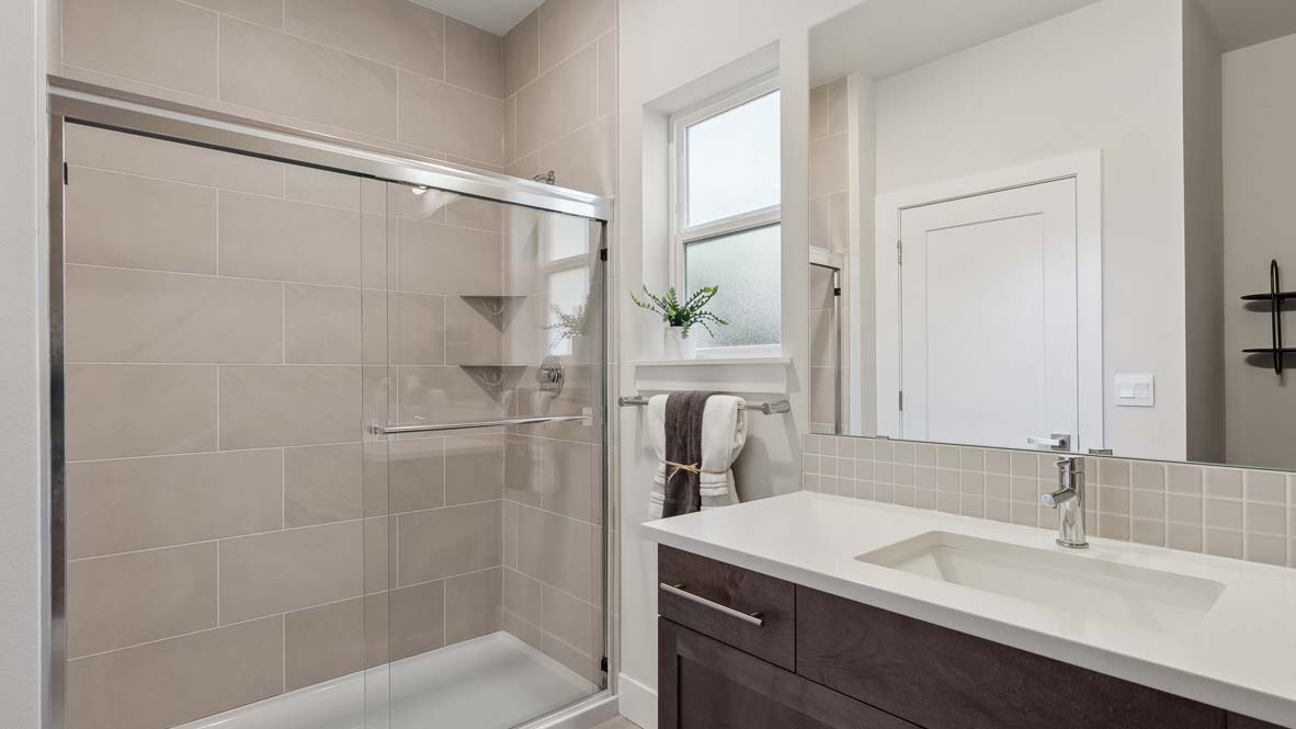 Modern bathroom with walk-in glass shower, single-sink vanity, and neutral tile finishes.