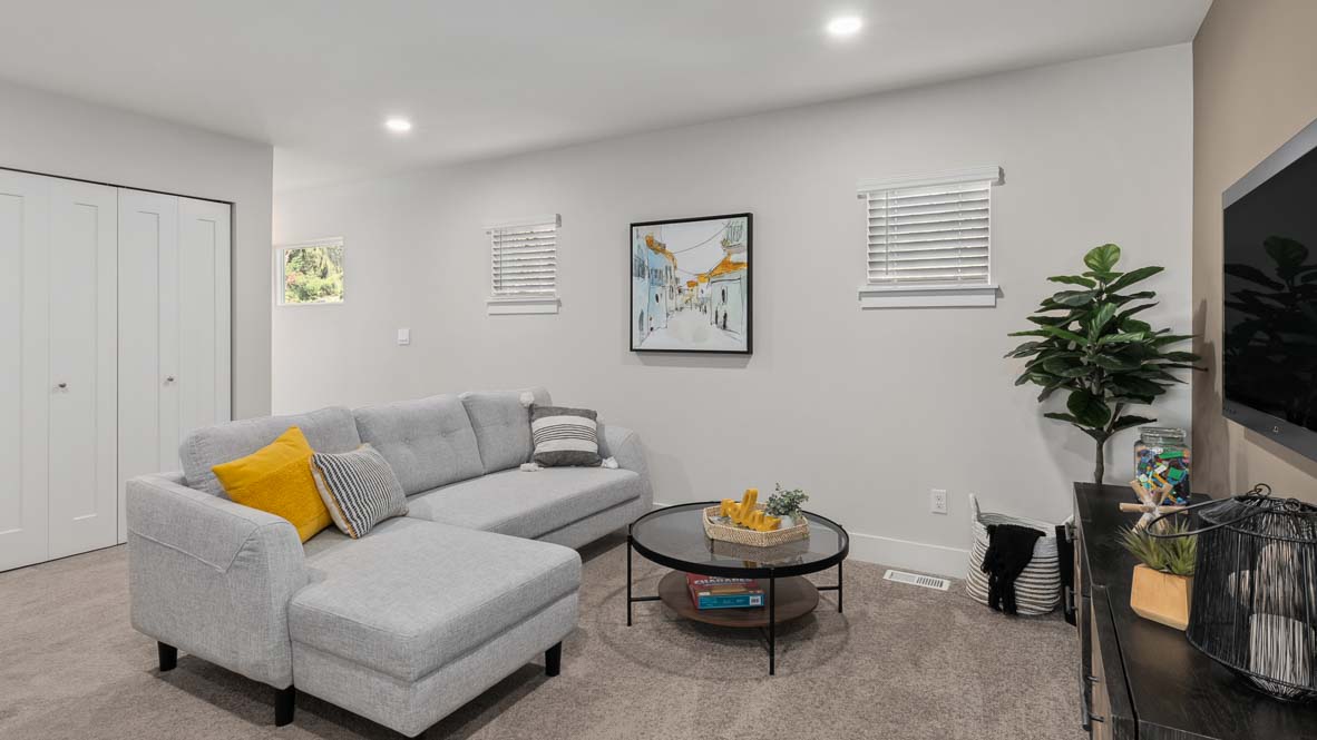 Spacious recreation room with sectional sofa, round coffee table, television, and multiple windows.