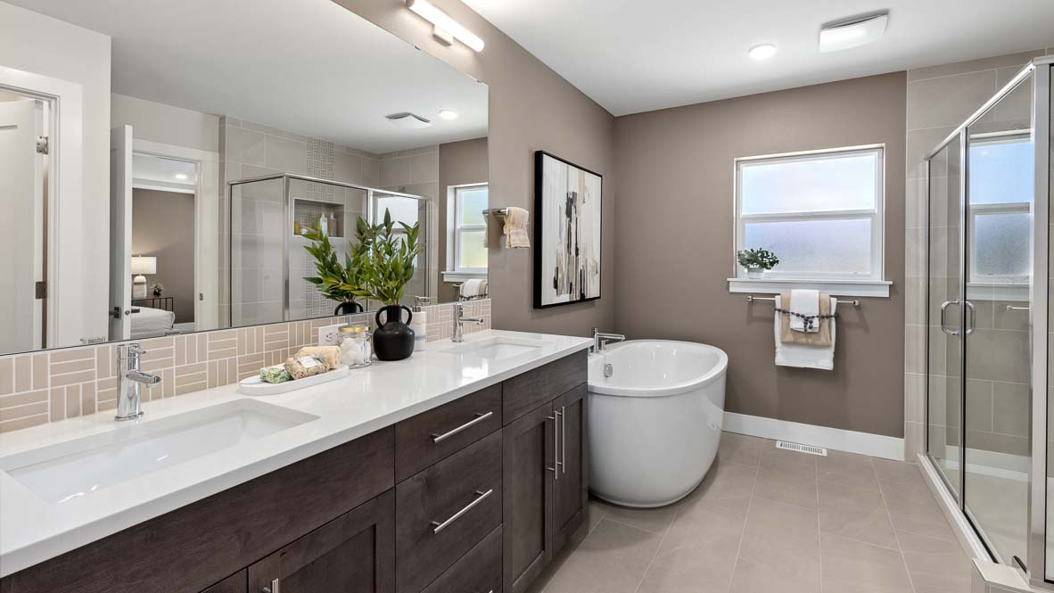 Primary bathroom with dual-sink vanity, freestanding soaking tub, glass shower, and tile flooring.