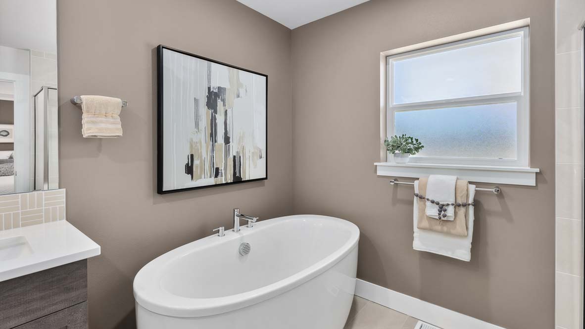 Freestanding soaking tub beneath frosted window in a spa-inspired primary bathroom.