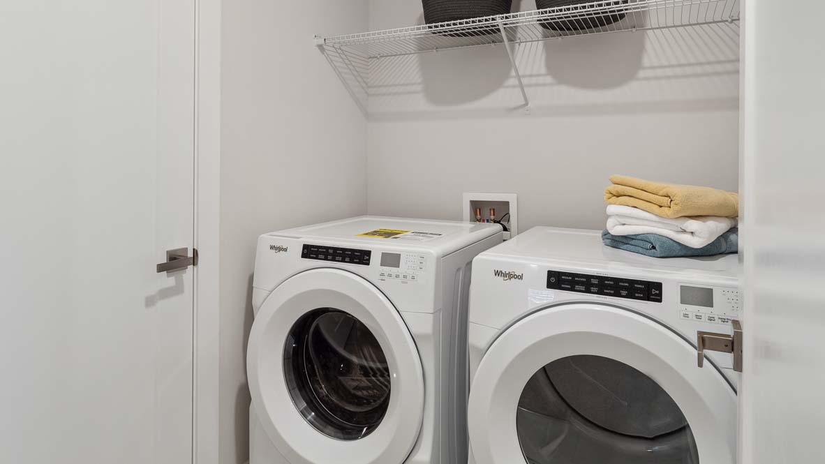 Laundry closet with front-loading washer and dryer, wire shelving, folded towels, and white interior walls.