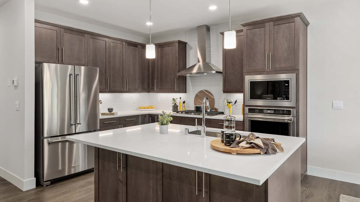 Contemporary kitchen with large white quartz island, dark wood cabinetry, stainless steel appliances, and pendant lighting.