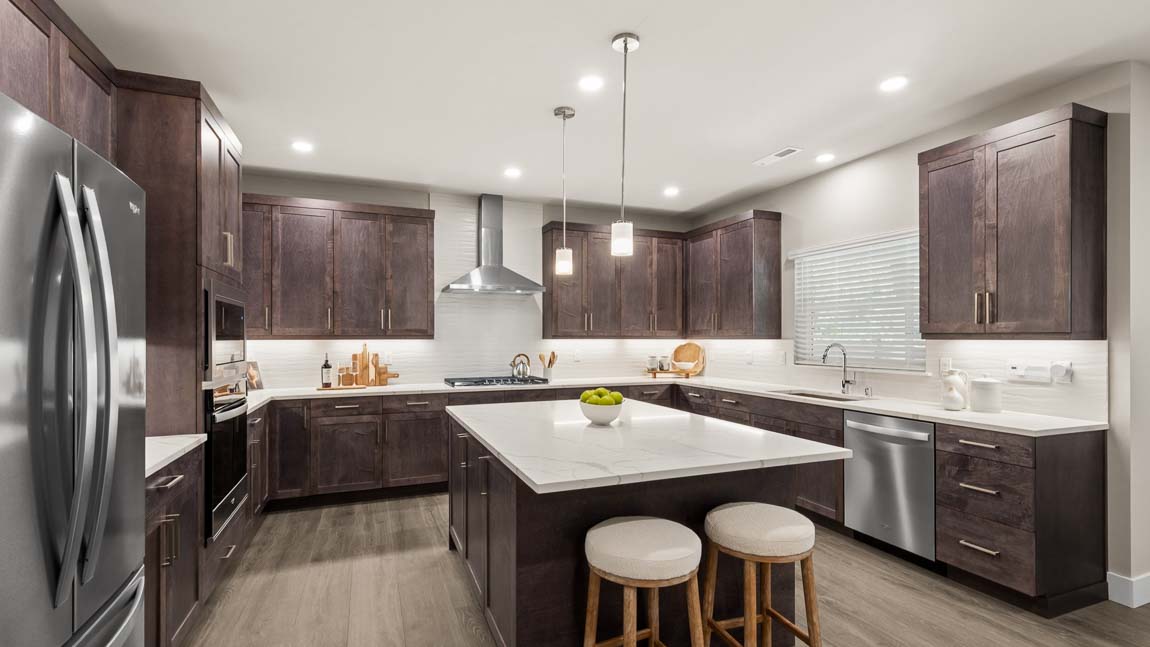Spacious gourmet kitchen with large quartz island, dark wood cabinetry, stainless steel appliances, and pendant lighting.