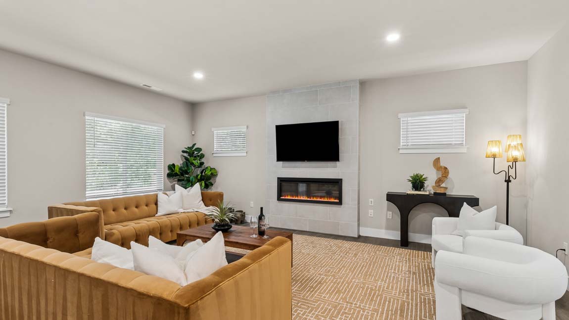 Living room with fireplace, mounted TV, upholstered seating, accent table, and large windows.