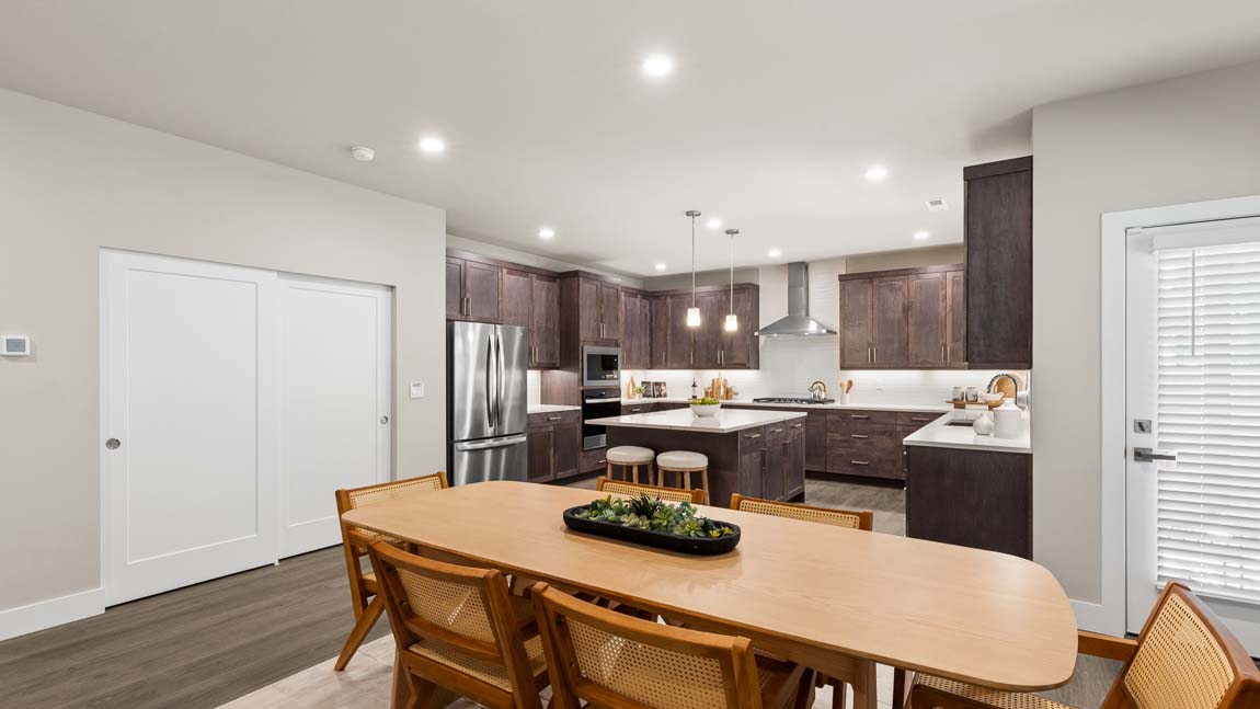 Dining area with wood table and woven chairs overlooking the adjacent kitchen.