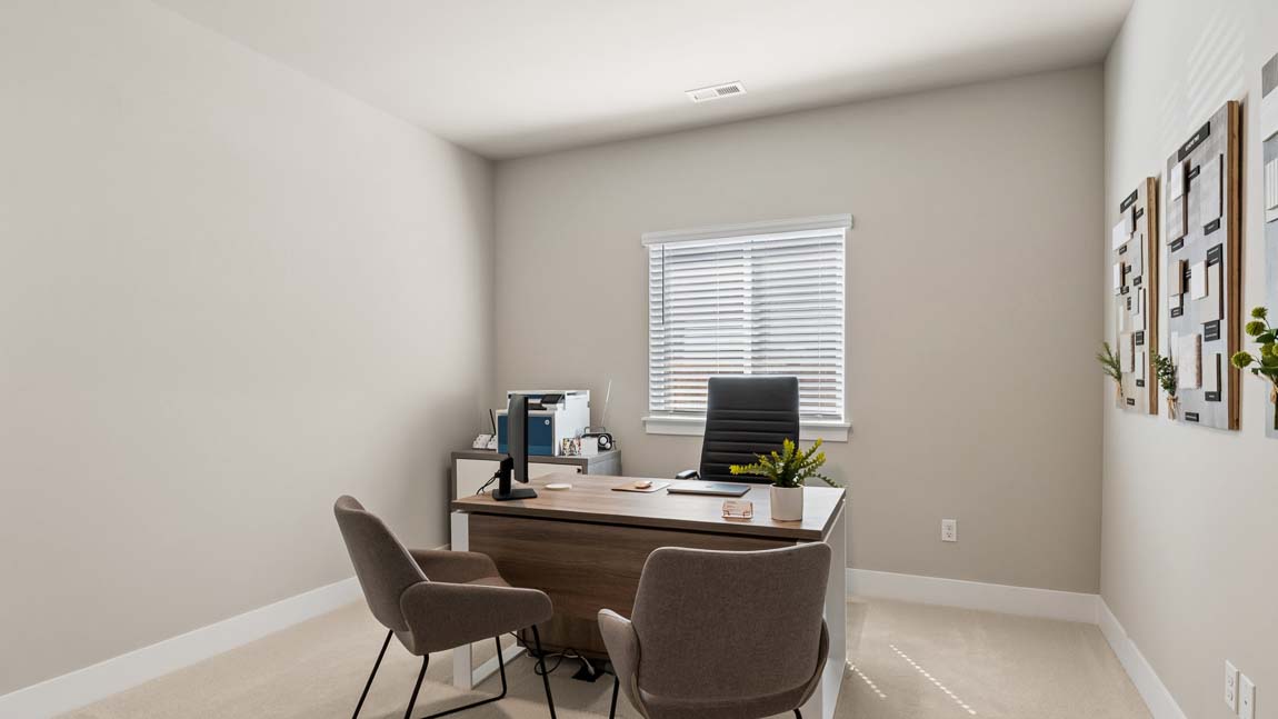 Home office with executive desk, guest chairs, window, and neutral wall décor.