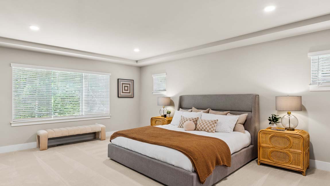 Expansive primary bedroom with upholstered bed, large window, tray ceiling, and coordinated furnishings.