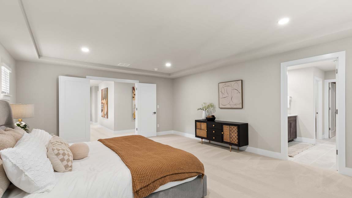 Primary bedroom with tray ceiling, large bed, sitting area, and entry to adjoining bathroom.