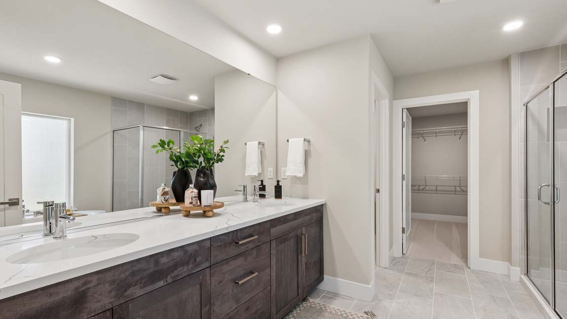 Primary bathroom with double vanity, large mirror, glass shower enclosure, and walk-in closet access.