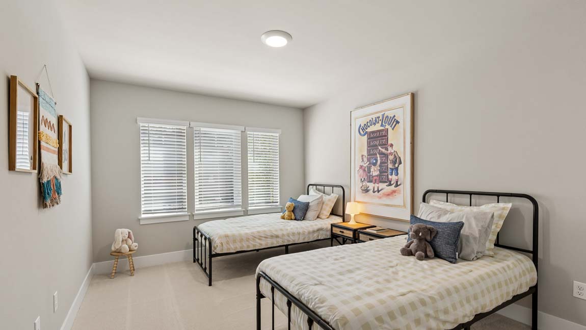 Children's bedroom with two twin beds, shared nightstand, stuffed animals, and large window.