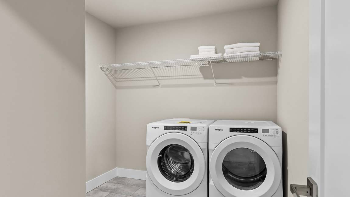 Laundry room with front-loading washer and dryer, wire shelving, tile flooring, and neutral painted walls.