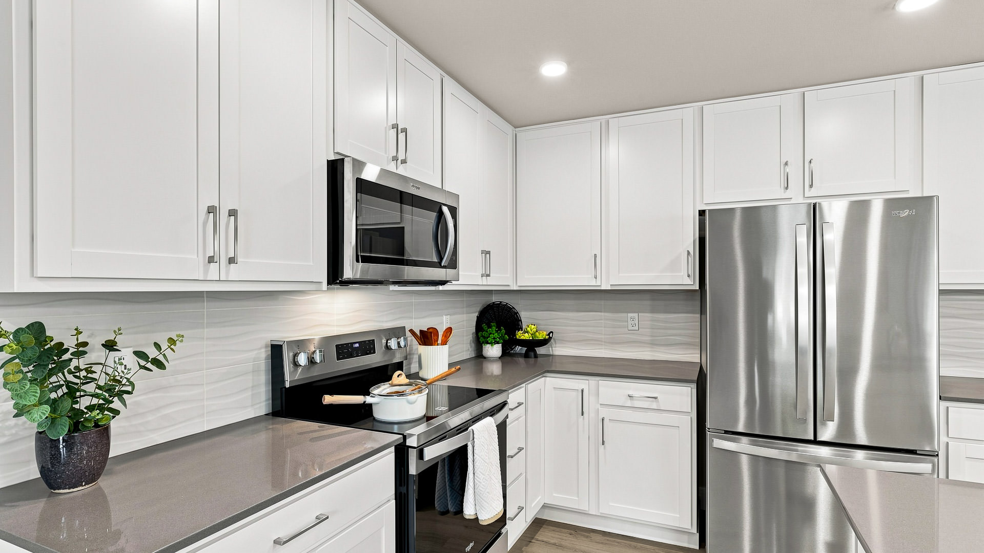 Close view of a white kitchen with gray counters, stainless steel range, microwave, and French-door refrigerator.